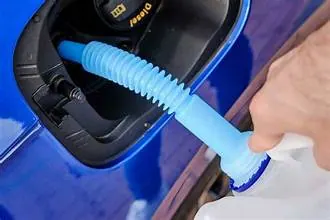 Pouring diesel exhaust fluid from a jug with a blue spout into a vehicle's DEF filler