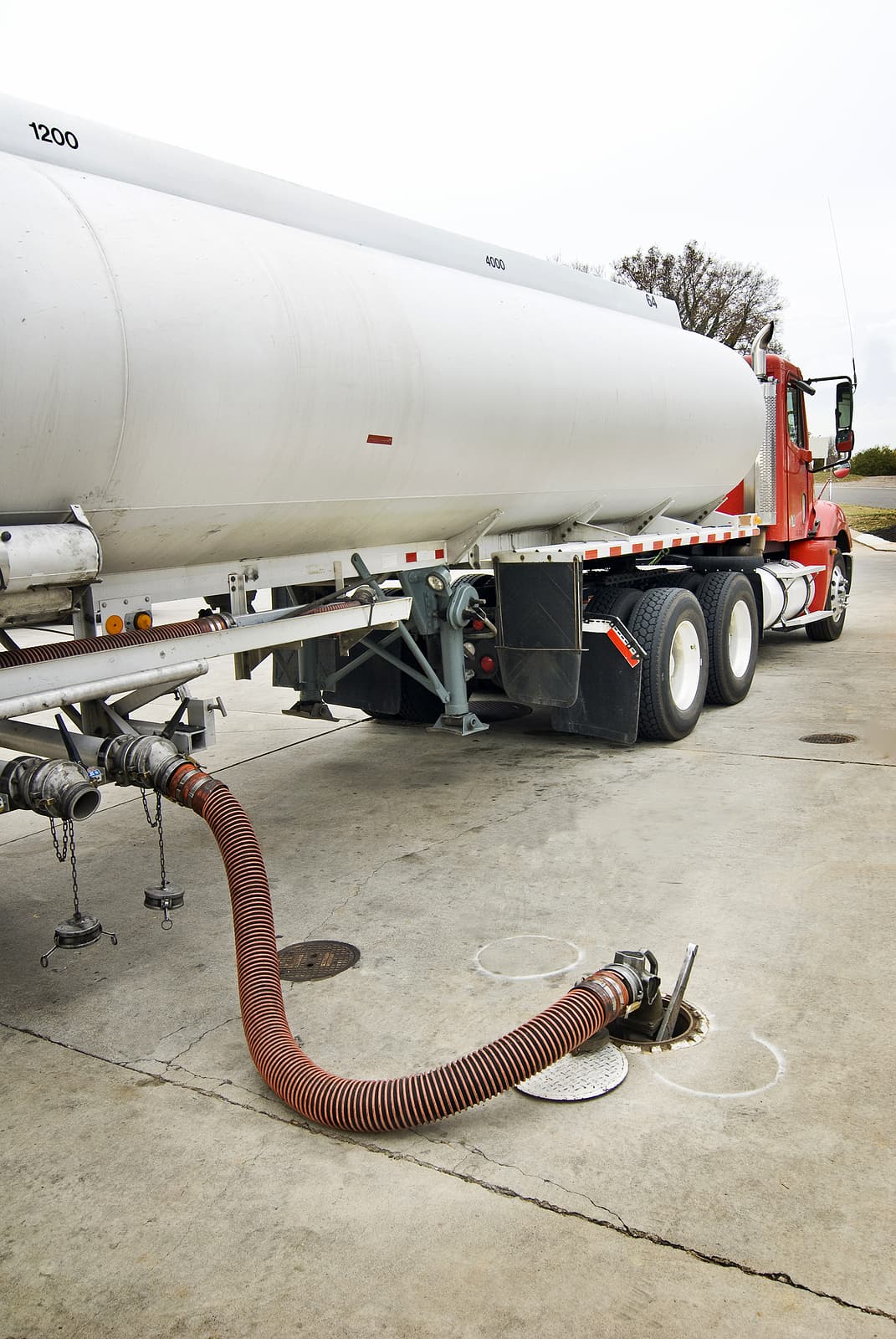 Tanker truck refilling an underground fuel storage tank through a delivery hose