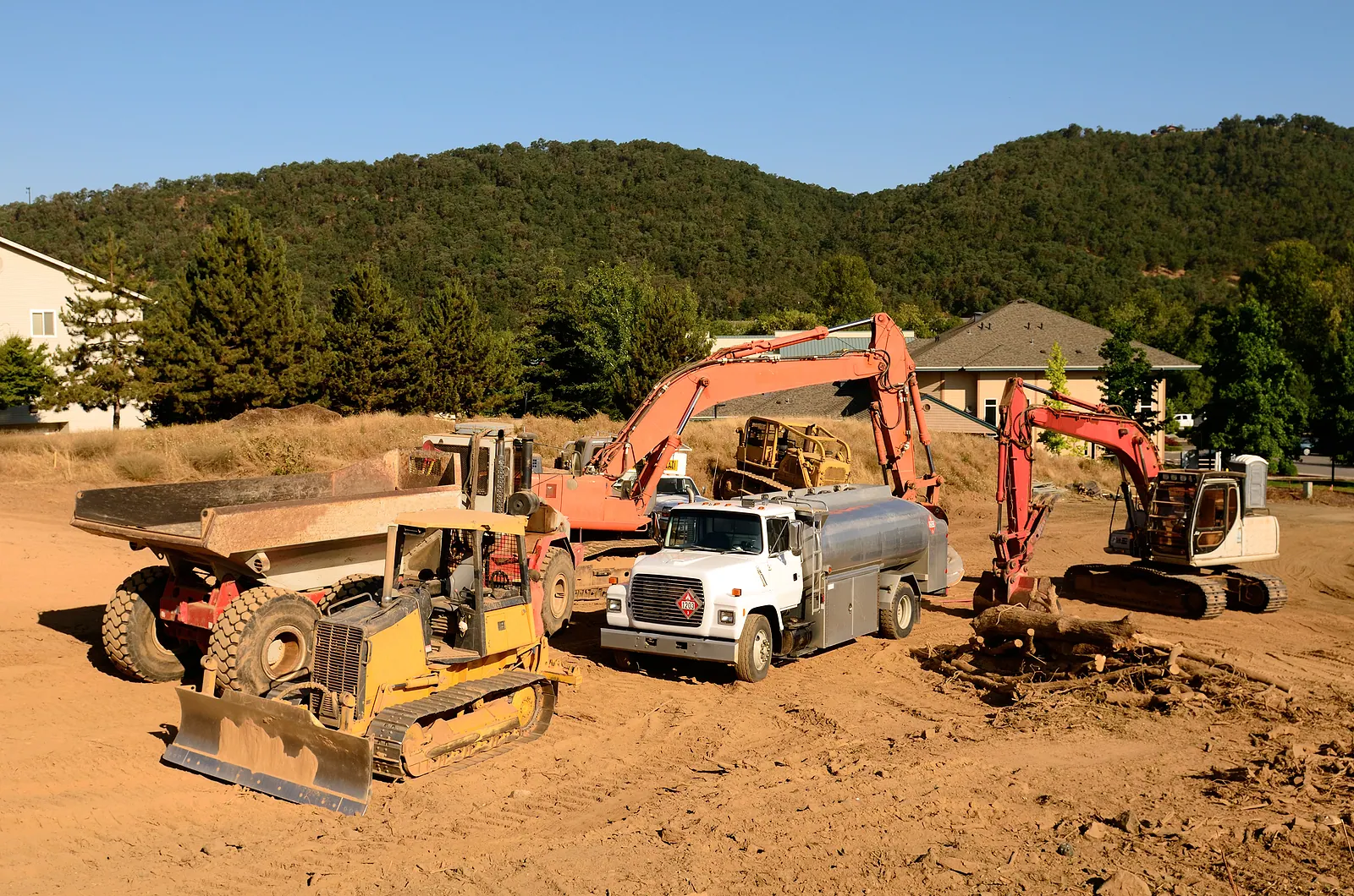 Fuel tank truck parked among a dozer, two excavators and an articulated dump truck on a graded dirt construction site