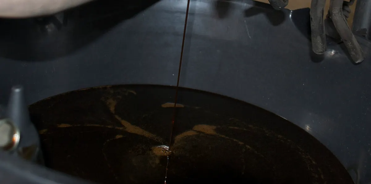 Dark used motor oil draining into a catch pan, the kind of waste oil black diesel is made from